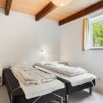 Zimmer mit zwei Betten, Holzdecke und Fenster mit Blick auf Bäume.