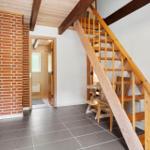 Holztreppe führt zur oberen Etage. Ziegelwand und Bodenfliesen sichtbar.