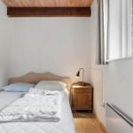 Schlafzimmer mit Bett, Nachttisch und Fenster. Holzdecke und Tür sichtbar.