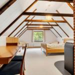 Dachgeschosszimmer mit Holzbalken, Bett, Tisch und Kaminwand.