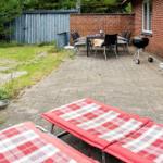 Terrasse mit Liegestühlen, Tisch, Stühlen und Grill. Hinterhof mit Holzzaun und Grünfläche.