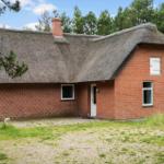 Rotes Backsteinhaus mit Strohdach und weißer Tür im Wald.
