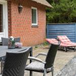 Terrasse mit Tisch, Stühlen, Liegen und Grill neben rotem Backsteinhaus.