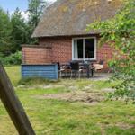 Rotes Backsteingebäude mit Strohdach und Gartenmöbeln. Grün umgeben mit Bäumen.