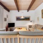 Wohnzimmer mit Holzdecke, Sofa und Fernseher. Fenster mit Blick auf Wald.