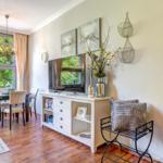 Ein Essbereich mit Tisch, Stühlen und großem Fenster. Fernseher auf weißem Schrank mit Dekoration.