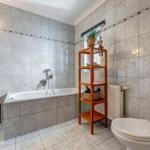 Badezimmer mit Badewanne, Toilette und Holzregal.