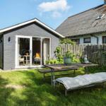 Garten mit Holztisch, Bank und Liege vor grauem Haus mit Glasfront.