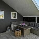 Terrasse mit Sitzgruppe, Tisch und Beleuchtung unter Dach.