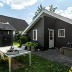 Haus mit Garten, Terrasse und Sitzgelegenheiten unter blauem Himmel.