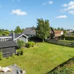 Grüner Garten mit Holzterrasse und Blick auf mehrere Häuser und Bäume.