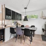 Essbereich mit Tisch, Stühlen und Kaminofen. Küche mit Kühlschrank und Schieferwand.