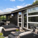 Terrasse mit Sitzgruppe, Tisch und Blumen. Haus mit Glasfront und Holzwand.