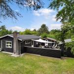 Schwarzes Ferienhaus mit Terrasse, Sonnenschutz und Garten. Umgeben von Bäumen und Grün.