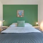 Schlafzimmer mit grünem Wandabschnitt, Bett mit Kissen und Nachttischen.