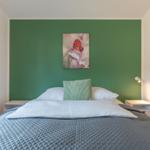 Schlafzimmer mit Bett, grüner Wand und Wandbild mit Schmetterling.