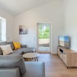 Wohnzimmer mit Sofa, TV und Fenster zur Außenseite.