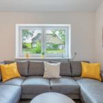 Grauer Ecksofa mit gelben und weißen Kissen vor Fenster mit Blick auf Dachhütte.