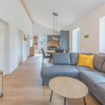 Wohn- und Essbereich mit grauem Sofa, Holzboden und großem Fenster.