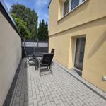Terrasse mit Tisch und Stühlen neben gelbem Haus mit Fenstern.