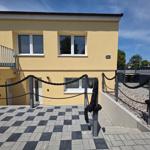 Gelbes Haus mit Balkon und schwarz-weißem Kiesweg. Eingang mit Seilzaun.