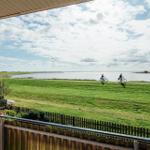 Von der Terrasse aus Blick auf grünes Feld und Wasser mit zwei Radfahrern.