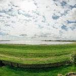 Grünes Feld mit Zaun, Blick auf Wasser und Himmel mit Wolken.