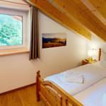 Schlafzimmer mit Holzbett, Fensterblick auf Wald und Holzdecke mit Balken.