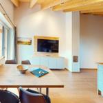 Essbereich mit Holztisch, Küche mit hellblauen Schränken und Wohnbereich mit Fernseher.