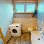 Badezimmer mit Waschmaschine, WC und Waschbecken. Holzfußboden und Fenster mit Blick.