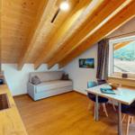 Wohnküche mit Sofa, Esstisch und Holzdecke. Blick auf den Garten.