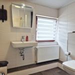 Bathroom with sink, mirror, toilet, and window with blinds.