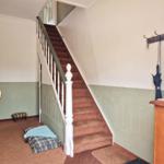 Staircase with wooden steps, wall paneling, and coat rack with umbrellas.