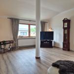 Living room with wooden floor, TV, grandfather clock, and window view.