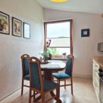 Dining area with table, chairs, and kitchen. Wall art and window view.
