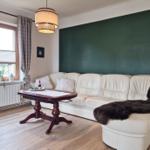 Living room with white sofa, dark green wall panel, and wooden floor.