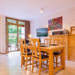 Essbereich mit Holztisch und Stühlen, Fernseher und Kabinett. Tür führt auf Balkon mit Gartenblick.