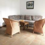 Wohnzimmer mit Sofa, zwei Rattanstühlen und Holztisch.