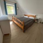 Schlafzimmer mit Holzbett, Fenster und Kleiderschrank.