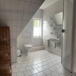Badezimmer mit Dusche, Waschbecken und WC unter Dachschrägen.