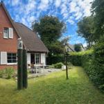 Rotes Backsteingebäude mit Terrasse und Garten unter blauem Himmel.