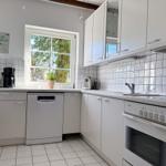 Küche mit weißen Schränken, Spüle, Herd und Fenster mit Blick nach draußen.