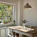 Esstisch mit Stühlen unter einem Hängelampen, Fensterblick auf Garten.