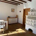 Esszimmer mit rustikalem Ofen, Holztisch und Stühlen. Deckenbalken und Fliesenboden.