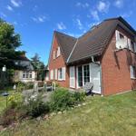 Rotes Backsteinhaus mit Garten und Terrasse unter blauem Himmel.