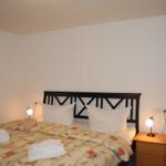 Schlafzimmer mit Bett, Nachttisch und Lampen. Fenster und Kleidung sind sichtbar.