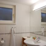 Badezimmer mit Waschbecken, Spiegel und Fenster.