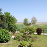 Garten mit Blumenbeeten und Zaun. Blick auf Felder und Horizont.