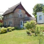 Haus mit Strohdach, Garten und Terrasse. Roter Holzrahmen und weiße Fenster.