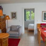 Wohn- und Essbereich mit Blick in Schlafzimmer. Holzmöbel, Wandbilder und Deckenleuchten.